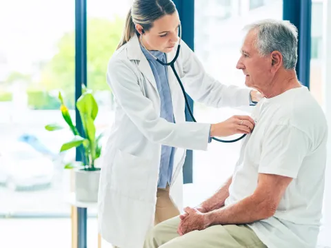 A female physician examining an older man's breathing with a stethoscope. 