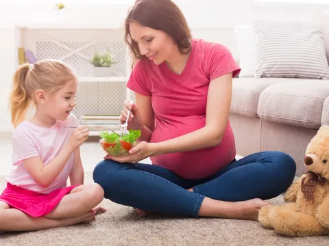Pregnant mother with daughter eating salad.