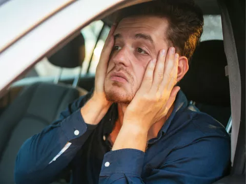 An upset man holds his face with his hands while sitting in a car.