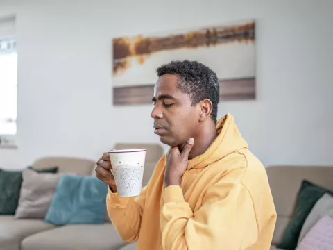 A man with a sore throat sips a cup of hot tea.