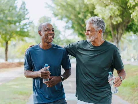 Two men walking outdoors together while holding water bottles.