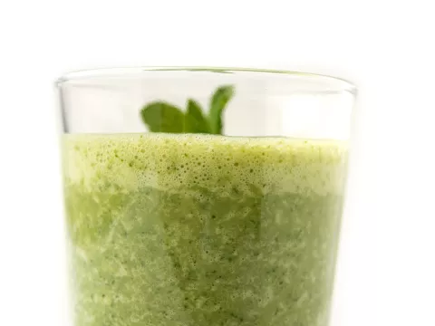 Clear glass of green smoothie with sprig on top.
