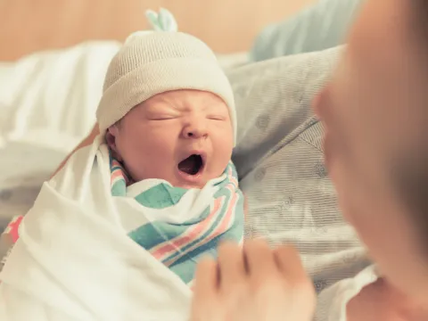 Newborn baby yawning in it's mother's arms