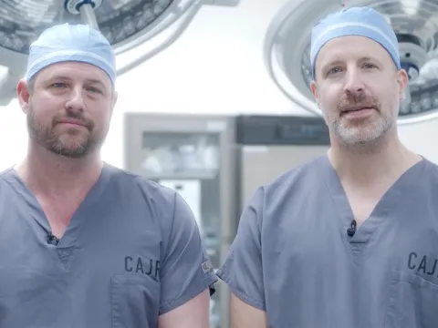 Two surgeons wearing scrubs and surgical caps standing together in an operating room.