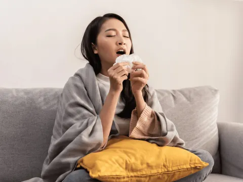 A woman sneezing into a tissue.