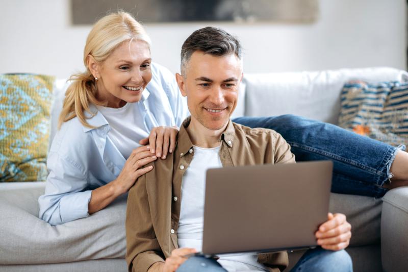A white mature couple in their living room and on their laptop