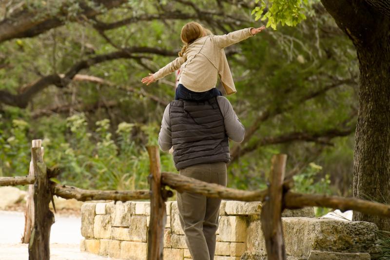 Father and daughter walking in the woods next to a fence.