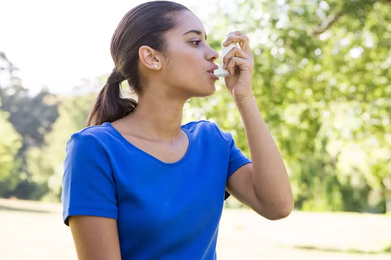 Young mixed-race woman using an asthma inhaler 