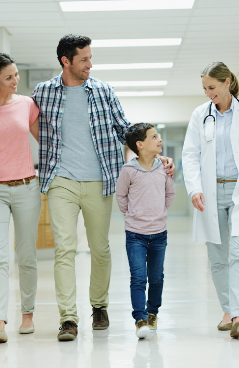 A Smiling Mother, Father and Son Walk Down a Hospital Hallway with a Doctor.