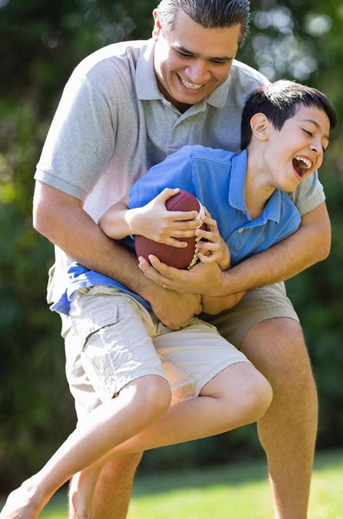 A father playfully tackles his son as they play football outside.