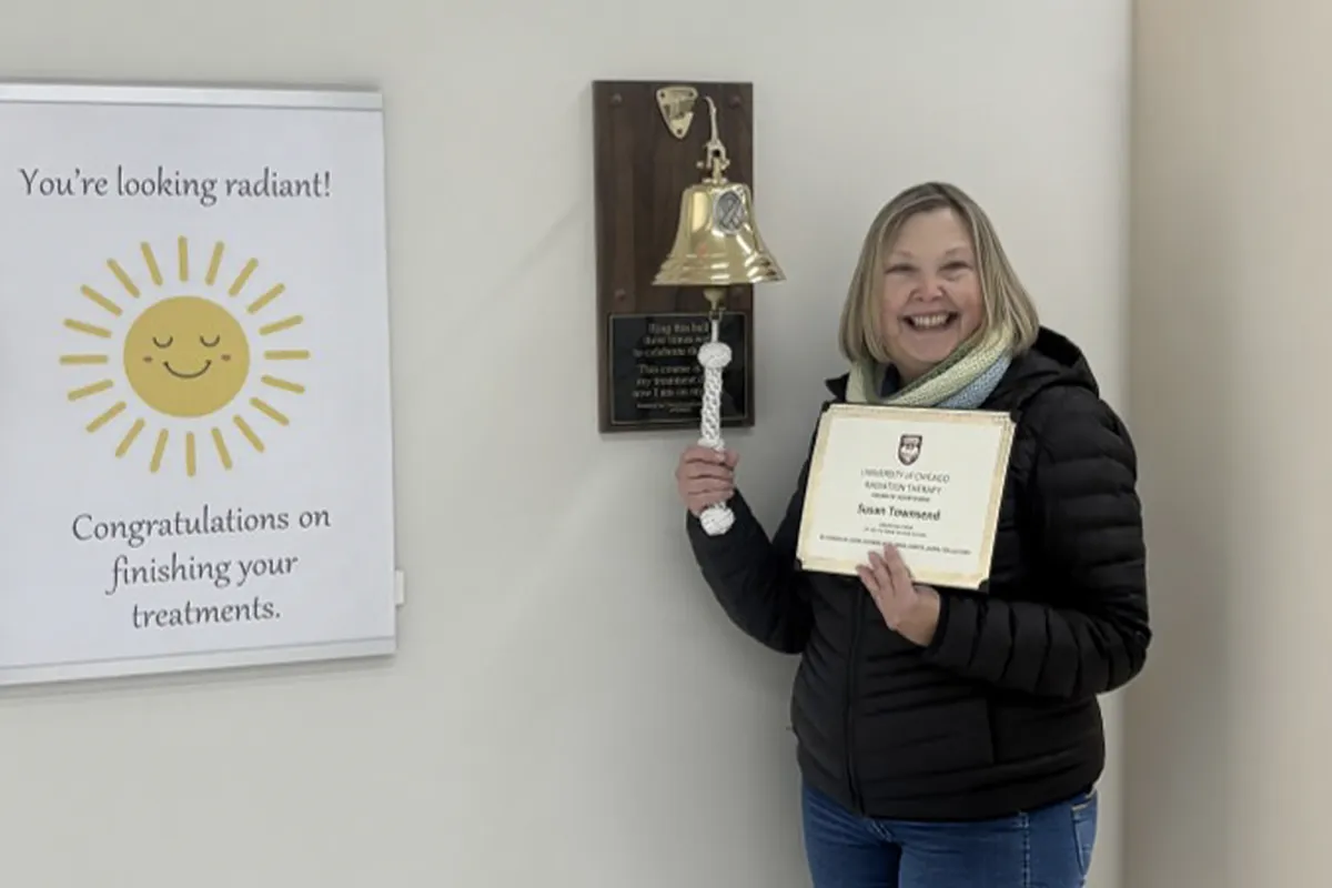 Smiling woman celebrating the completion of her radiation treatments by ringing a bell and holding a certificate.